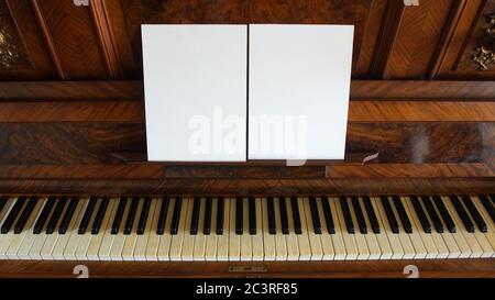 Vista frontale di un antico pianoforte in legno con la tastiera aperta e due fogli di carta bianca su supporto per note musicali Foto Stock