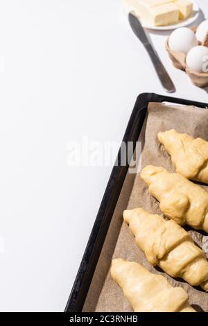 focalizzazione selettiva dei croissant grezzi sulla griglia da forno vicino al burro, alle uova, al coltello su sfondo bianco Foto Stock