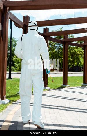 uomo di lavoro in tuta di nocciolo e respiratore disinfettando la costruzione in legno nel parco durante la pandemia di coronavirus Foto Stock