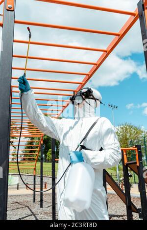 uomo di lavoro in tuta e respiratore disinfettante il terreno sportivo nel parco durante la pandemia covid-19 Foto Stock