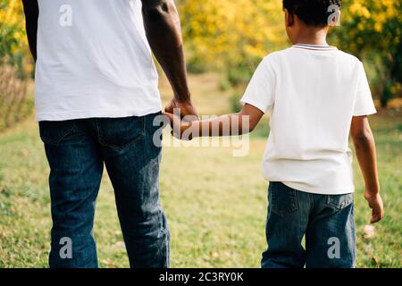 Padre e figlio afro-americano che tiene le mani nel parco all'aperto durante l'estate. Paternità e felice famiglia tempo insieme concetto Foto Stock