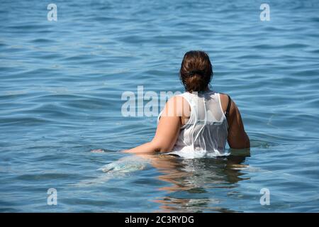 Vista ravvicinata dal retro della donna con i capelli scuri che si trova in una tranquilla acqua blu oceano. Foto Stock