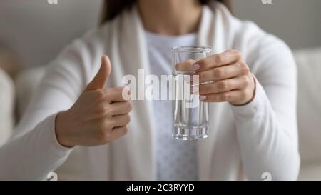 Donna che tiene un bicchiere d'acqua che mostra i pollici in vista del primo piano Foto Stock
