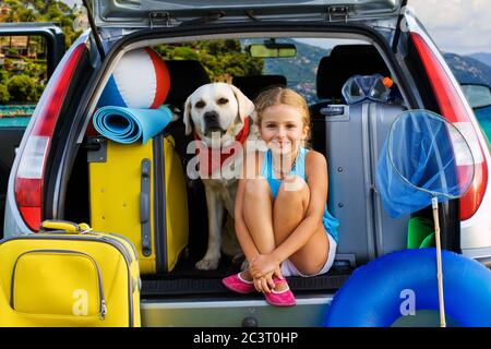 La ragazza giovane ha la valigia nel bagagliaio di un'auto in vacanza Foto Stock