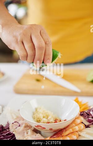 Immagine ravvicinata della donna che stringe metà del lime fresco in una ciotola con aglio a cubetti e paprika Foto Stock