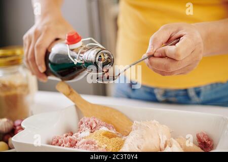 Mani di persona che aggiungono il cucchiaio di salsa di soia nel recipiente con la carne macinata Foto Stock