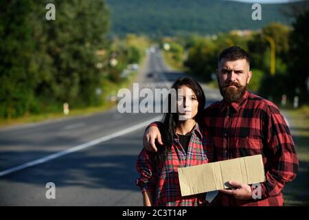 Uomo e donna cercano di fermare l'auto con un cartello di cartone. Avventura e hitchtrekking concetto. Coppia con volti stanchi viaggia con auto stop. Coppia innamorata viaggiando su hitchtrekking, spazio copia. Foto Stock