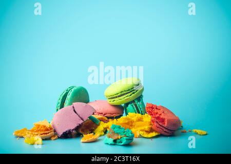 Biscotti macaroon colorati rotti su sfondo blu. Dolci, dessert e dolci festosi e luminosi. Cottura sfondo Foto Stock