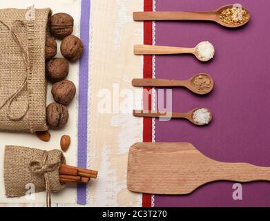 Spezie naturali, fogli di carta e nastri, spazio per la copia. Concetto di SPICE. Ingredienti sani su sfondo di tessitura di legno chiaro. Sacchetto con noci, noci, cannella, cucchiai di cacao, zucchero, sale, vista dall'alto. Foto Stock