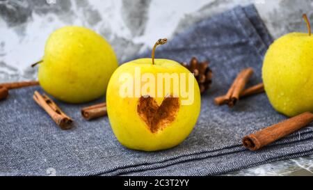 Mele dorate verdi o Granny smith forma di cuore tagliata sulla mela con bastoncini di cannella su asciugamano da cucina, preparazione di cibo, dessert Foto Stock