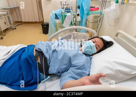 Giovane donna cinese asiatica in contraction pain sul letto di reparto della stanza di lavoro dell'ospedale in attesa di parto neonato Foto Stock