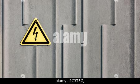 Segno di alta tensione su una superficie metallica grigia. Simbolo di pericolo elettrico su un segnale di avvertenza su sfondo grigio Foto Stock