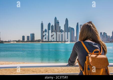 Giovane donna che guarda il Dubai Marina dalla spiaggia di Palm Jumeirah durante una giornata di sole, Dubai, Emirati Arabi Uniti Foto Stock