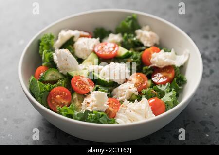 Insalata con kale, pomodori, cetrioli e mozzarella in ciotola bianca Foto Stock