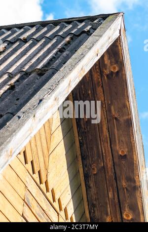 Parte della facciata vecchia e rurale casa marrone con tetto in cielo blu con sfondo nuvole bianche Foto Stock