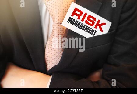Parole di gestione del rischio su una carta nella tasca superiore del vestito dell'uomo d'affari. Uomo che tiene una carta con un testo di messaggio scritto su di essa. Rischi di investimento aziendale Foto Stock