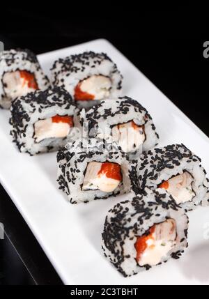 Rotolo di sushi uramaki con salmone, anguille affumicate, cetriolo, formaggio cremoso e semi di sesamo su un piatto bianco. Foto Stock
