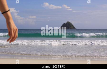 Mano di donna e sfondo onda alla spiaggia di Mawun. Kuta Lombok è un paradiso esotico sull'isola indonesiana, con belle spiagge di sabbia bianca e cr Foto Stock