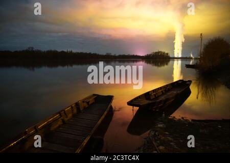 Luce surreale dalle case verdi e vapore dalla centrale elettrica che si riflette nel fiume Loira, Francia con vecchie barche in legno piano di notte Foto Stock