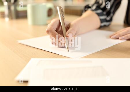 Primo piano di mani donna che scrivono lettera seduta su una scrivania Foto Stock