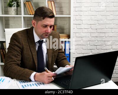 Un uomo d'affari legge i documenti di affari mentre si siede ad una scrivania dell'ufficio. Foto Stock
