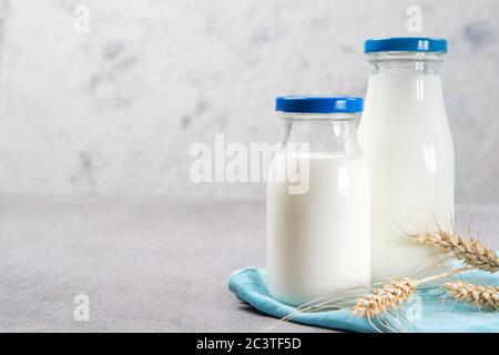 Due bottiglie di latte scremato fresco con tappi blu e asciugamano blu su un tavolo di pietra luminoso Foto Stock