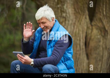 Ritratto di un uomo anziano attivo sorridente allo smartphone e che sventola in videochiamata durante l'escursione, spazio di copia Foto Stock