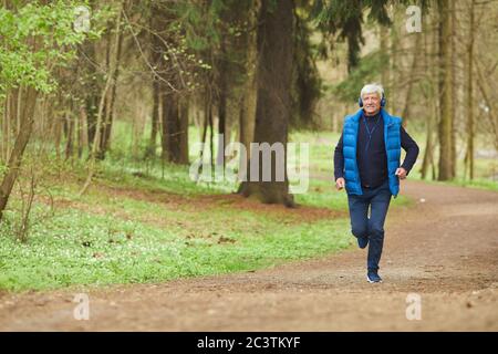 Ritratto grandangolare di un uomo anziano attivo che ascolta la musica mentre corre nella bella foresta autunnale, copia spazio Foto Stock