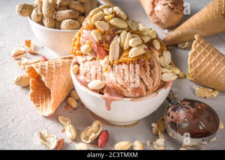 Gelato al burro di arachidi. Gelato alle arachidi dolci con farcitura al burro di arachidi e molte arachidi, su fondo grigio con coni di cialda di icecream Foto Stock