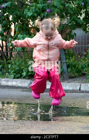 Bambino felice che salta in puddle in cappotto impermeabile. Una ragazza si diverte in tempo piovoso in un impermeabile luminoso. Foto Stock