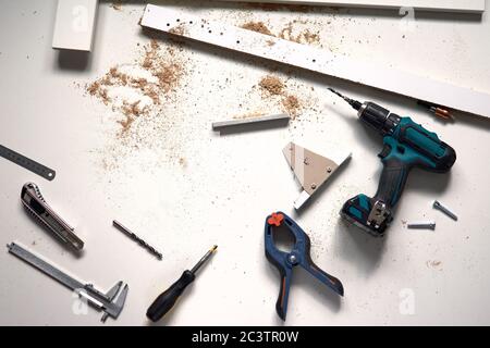 Uomo che lavora a casa per lavori di ristrutturazione, forando con un cacciavite. Gruppo di attrezzi di riparazione su fondo bianco in legno. Foto Stock