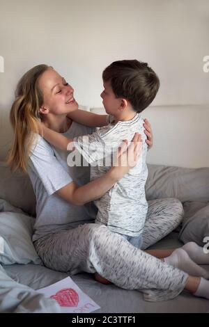 Buon giorno della madre. Bambino ragazzo si congratula con la mamma e dà i suoi tulipani fiori e cartolina. Mamma e figlio sorridono e abbracciano Foto Stock