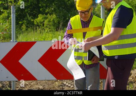 Pianificazione e implementazione del lavoro di squadra. Ingegnere e lavoratore in caschi in un cantiere. Una metafora aziendale per il consenso, il successo e il raggiungimento Foto Stock