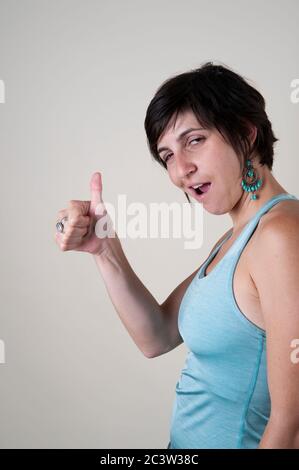 Studio girato di una modella sorridente femminile nel suo 20s dà i pollici su sfondo bianco Foto Stock
