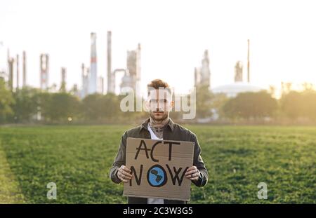 Giovane attivista con placche in piedi all'aperto da raffineria di petrolio, protestando. Foto Stock