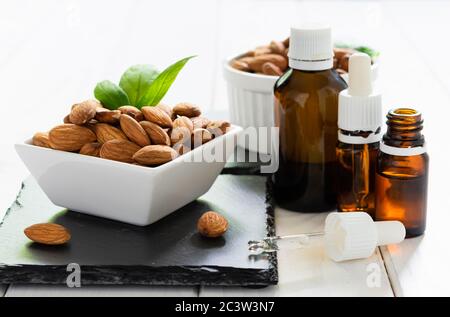 mandorle in un piatto bianco e bottiglie di vetro con olio su un vassoio nero su un tavolo di legno Foto Stock