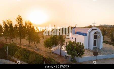 Vista aerea del tramonto e simbolo bianco dipinta cappella moderna arco di Agia Triada, Protaras, Famagosta, Cipro dall'alto. Vista dall'alto del turista Foto Stock