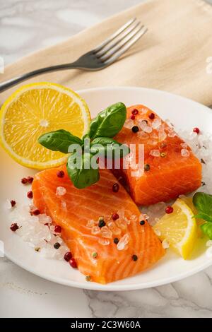 Fette di trota leggermente salate con spezie, basilico e limone su un piatto bianco Foto Stock
