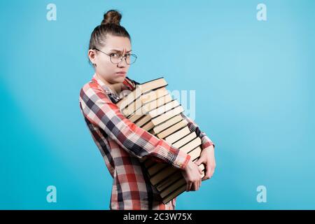 Triste giovane studente in occhiali detiene un gran numero di libri nelle sue mani Foto Stock