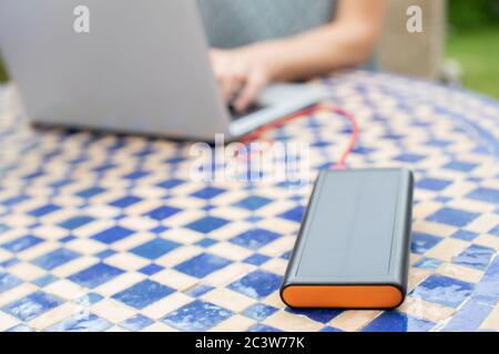Donna che carica il computer portatile all'aperto a casa con la Banca di alimentazione solare portatile Foto Stock