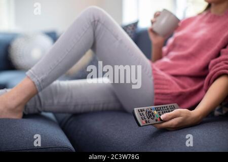 Dettaglio della donna rilassante sul divano tenendo premuto il telecomando e guardare la televisione Foto Stock