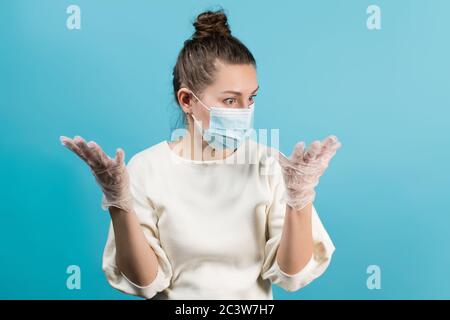 Una donna in una maschera medica le guarda le mani con guanti medici in shock Foto Stock