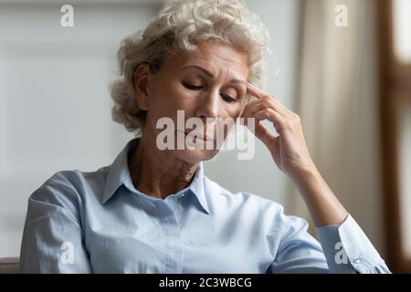 La donna anziana sembra preoccupata seduta in interni pensando ai problemi di vita Foto Stock