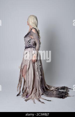 Ritratto di bionda ragazza che indossa strappato vecchio abito da sposa a lunghezza intera in piedi posa, isolato contro uno sfondo studio. Foto Stock