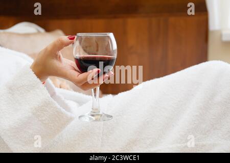 Una mano di donna tiene un bicchiere di vino rosso in una tinta bianca Foto Stock