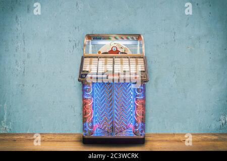 Jukebox vintage colorato di fronte a una parete blu con intemperie su un pavimento di legno Foto Stock