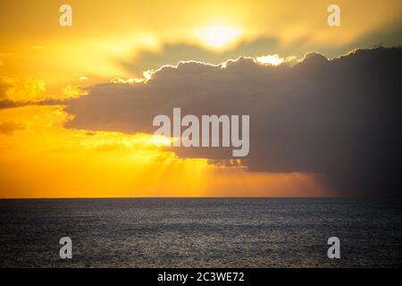 Luce dai raggi del sole che trafano le nuvole scure e drammatiche sul mare al tramonto Foto Stock