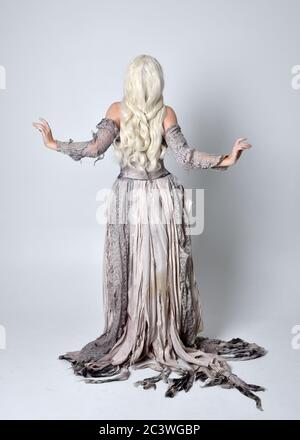 Ritratto di bionda ragazza che indossa strappato vecchio abito da sposa a lunghezza intera in piedi posa, isolato contro uno sfondo studio. Foto Stock