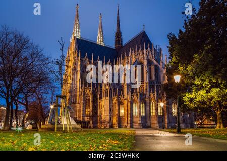 Vista notturna della chiesa votiva (Votivkirche) a Vienna, Austria. Parco cittadino in autunno con vicoli illuminati da lampioni di strada e una bella cattedrale gotica Foto Stock