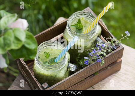 Frullato verde su vecchio sgabello vicino fiori sulla natura. Concetto di cibo sano Foto Stock